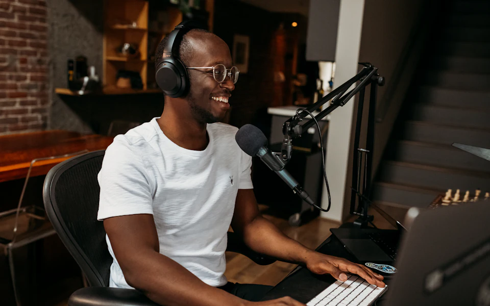 Smiling man with headphones practising speaking into a microphone at his desk