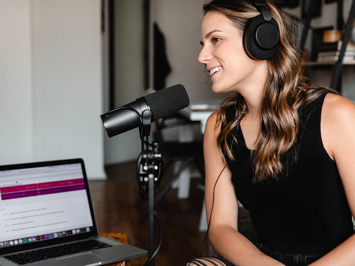 Smiling woman wearing headphones, speaking into a podcast microphone